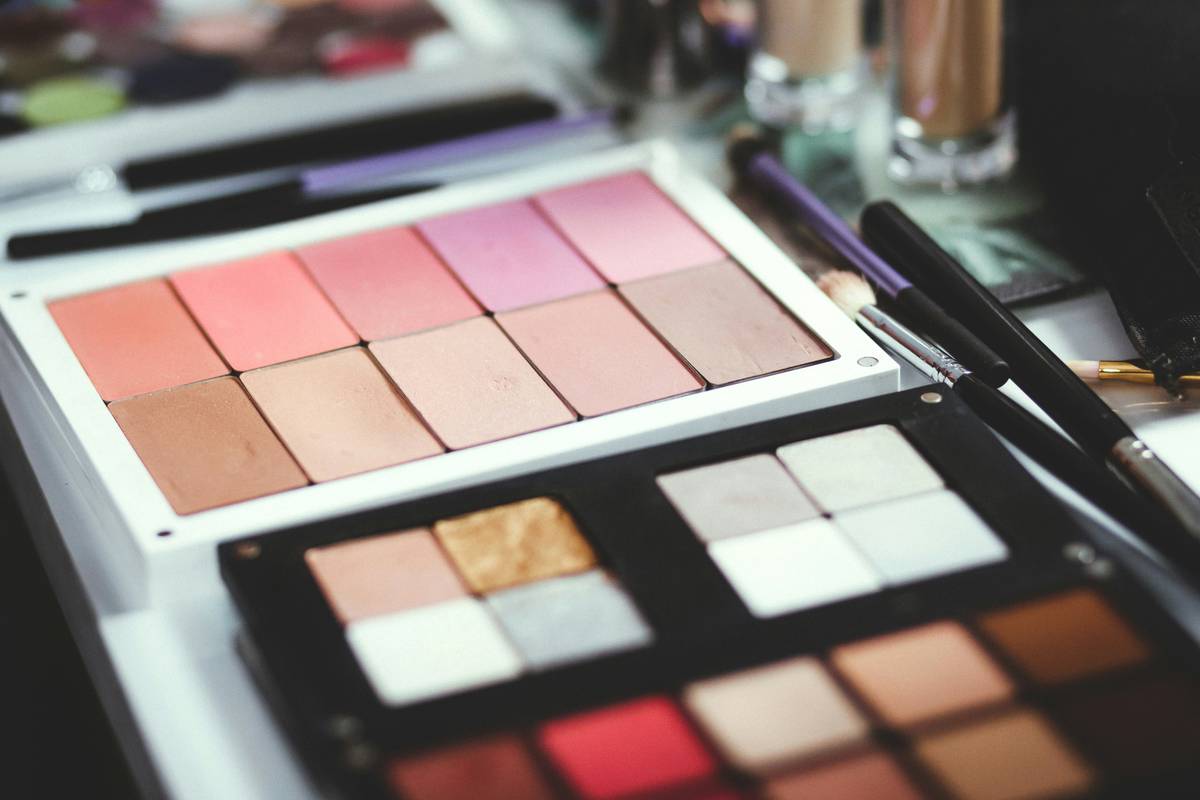 A hand holding a lightweight blush palette with multiple soft pink and peach shades arranged neatly in a compact